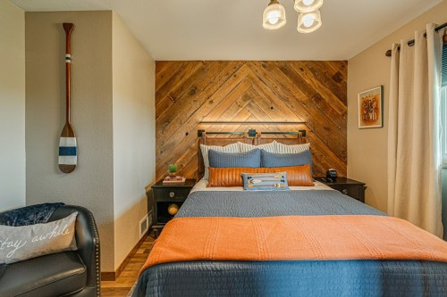 Cozy bedroom featuring a wooden accent wall, a bed with orange and blue bedding, and a decorative paddle.