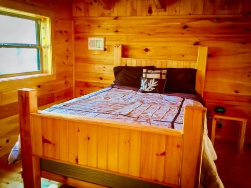 Cozy wooden bedroom featuring a bed with a quilt, decorative pillows, and a window letting in natural light.