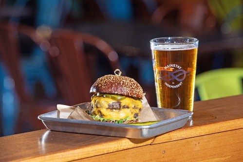 A juicy cheeseburger with pickles on a sesame seed bun, served with a pint of beer on a wooden table.