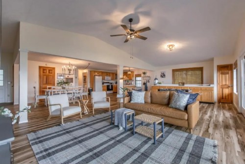 Spacious living area with a brown sofa, wooden dining table, and modern kitchen, featuring light wood floors and a ceiling fan.