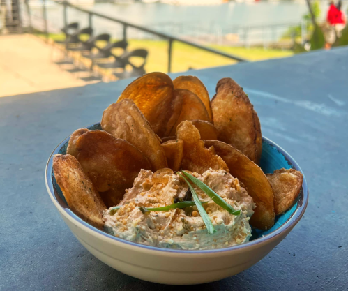 A bowl of creamy dip surrounded by crispy potato chips, with a scenic outdoor view in the background.