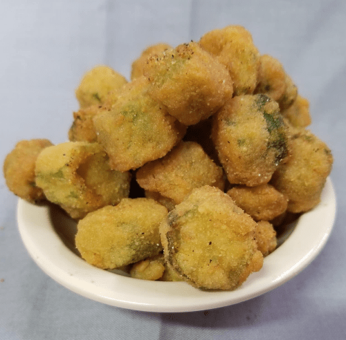 A white bowl filled with golden-brown, crispy fried okra pieces stacked high.