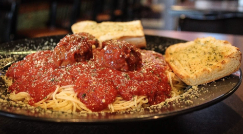 A plate of spaghetti topped with meatballs and marinara sauce, served with garlic bread on the side.