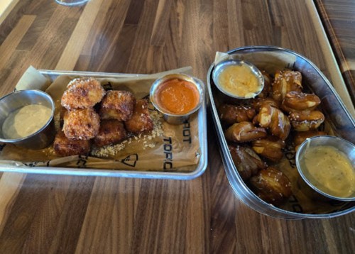 A platter with two types of appetizers: golden-brown fried bites with dipping sauces and soft pretzel bites with mustard.