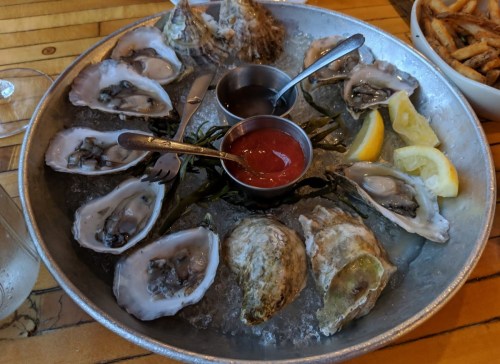 A platter of fresh oysters on ice, served with lemon wedges and dipping sauces.