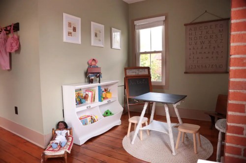 A cozy children's corner with a small table, chairs, books, a doll, and educational wall decor.