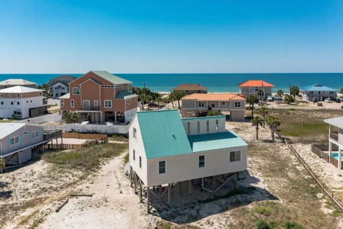 Aerial view of beach houses near the ocean, featuring colorful roofs and sandy surroundings under a clear blue sky.