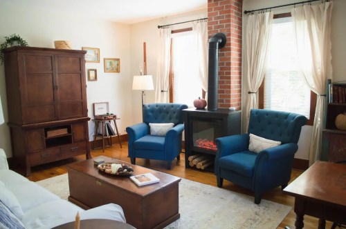 Cozy living room with blue armchairs, a wooden coffee table, and a stove, featuring warm lighting and decorative accents.