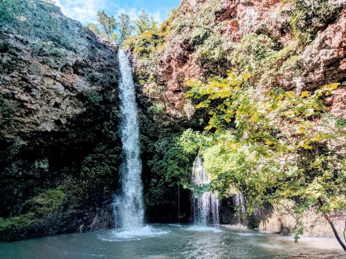 A scenic waterfall cascading down rocky cliffs into a serene pool, surrounded by lush greenery and trees.