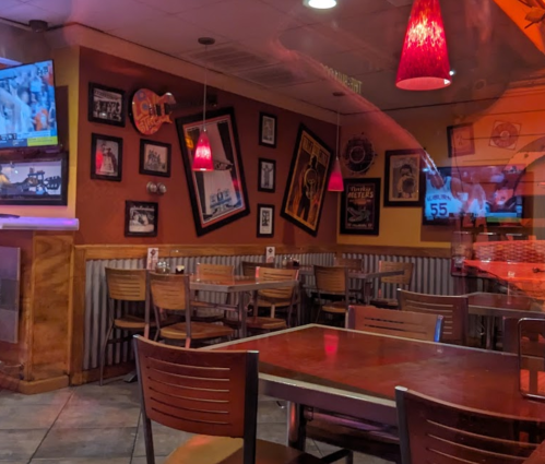 A cozy restaurant interior with wooden tables, chairs, and framed memorabilia on the walls, illuminated by red pendant lights.