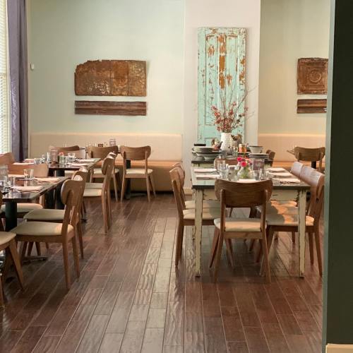 A cozy restaurant interior with wooden tables, chairs, and decorative wall art in soft green tones.