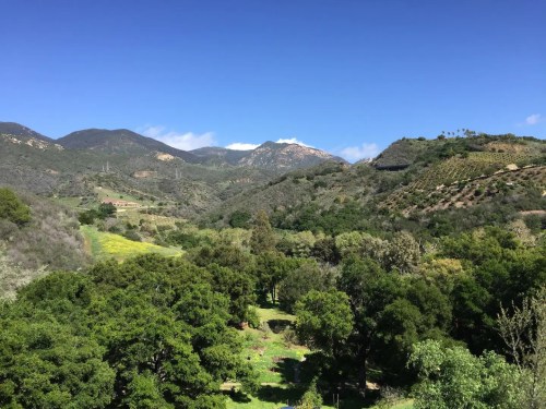 Lush green landscape with rolling hills and mountains under a clear blue sky.