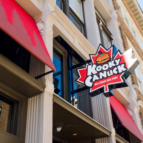 Sign for "Kooky Canuck" featuring a burger and maple leaf, with red awnings above a storefront.