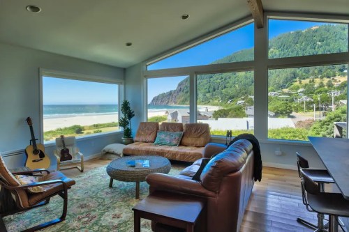 Cozy living room with large windows showcasing a beach view, featuring a guitar, sofa, and a round coffee table.