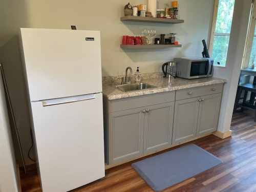 A modern kitchen corner featuring a white fridge, sink, microwave, and shelves with various kitchen items.