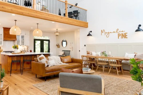 Bright, modern living space with a cozy sofa, dining area, and wooden accents, featuring a sign that reads "Meganlie Pine."