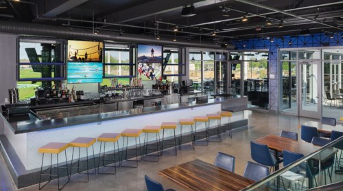 Modern bar area with high stools, large windows, and a vibrant mural, featuring a TV and a spacious dining area.