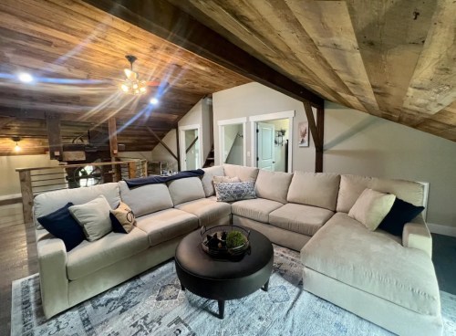 Cozy living room with a large sectional sofa, round coffee table, and wooden ceiling beams in a stylish attic space.