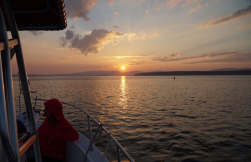 A serene sunset over calm waters, with a person in a red hoodie sitting on a boat, enjoying the view.