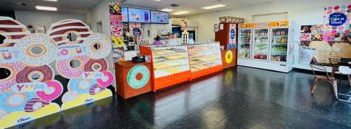 Bright donut shop interior featuring colorful decor, a display case of donuts, and a beverage fridge.