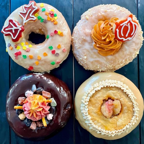 Four colorful donuts: one with sprinkles, one with frosting, one with candy toppings, and one with a cream filling.