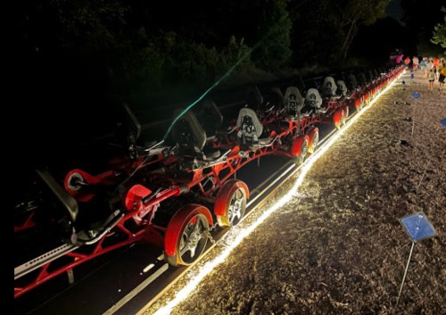 A long, illuminated ride with multiple seats on a dark path, surrounded by trees at night.