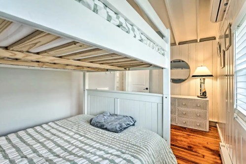 Cozy bedroom featuring a lofted bed, soft bedding, a dresser, and a lamp in a bright, airy space.