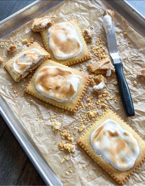A tray with four toasted pastries, some broken, scattered crumbs, and a knife on parchment paper.