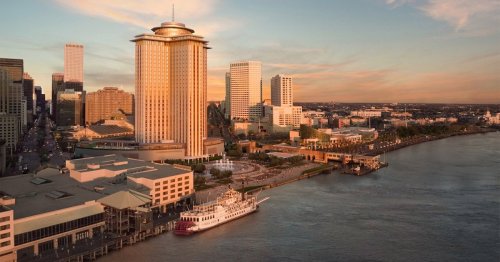 Aerial view of a city skyline at sunset, featuring tall buildings and a riverboat along the waterfront.