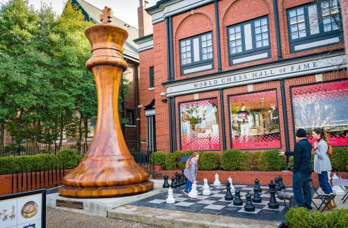 A giant wooden chess piece stands outside the World Chess Hall of Fame, with visitors playing on a large chessboard.