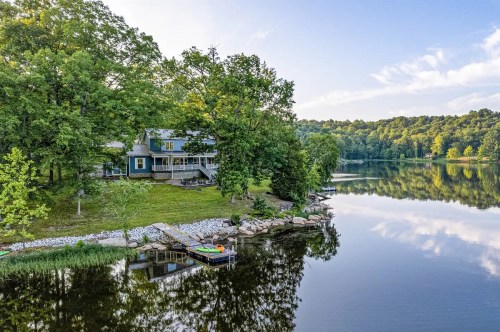 A serene lakeside view featuring a house surrounded by trees, with a dock and calm water reflecting the sky.