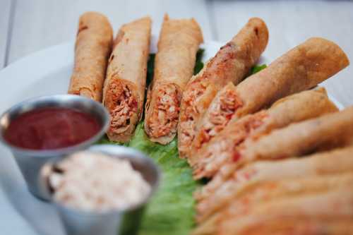 A plate of rolled tortillas filled with shredded chicken, served with dipping sauces on a bed of lettuce.