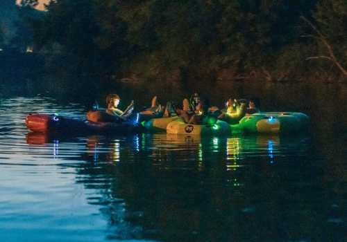 A group of people on colorful inflatable rafts at night, illuminated by lights, floating on a calm river.