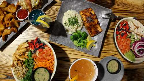 A spread of colorful dishes including salads, salmon, mashed potatoes, and appetizers on a wooden table.