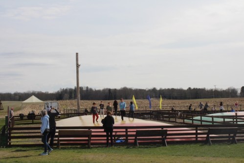 A group of people enjoying a dance or activity on a colorful outdoor platform, surrounded by fields and flags.