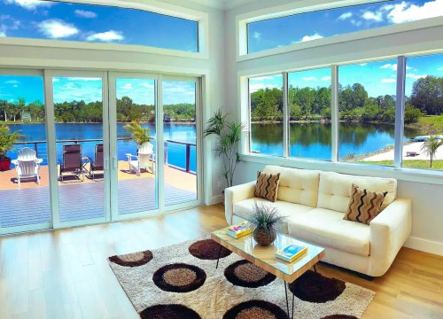 Bright living room with a white sofa, coffee table, and large windows showcasing a scenic lake view.