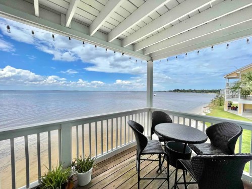 A scenic view from a balcony overlooking a calm body of water, with a table and chairs set for relaxation.