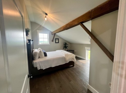 Cozy attic bedroom with a bed, wooden beams, and a window, featuring warm lighting and simple decor.