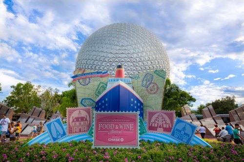 Epcot's iconic Spaceship Earth with a colorful Food & Wine Festival display in the foreground and a blue sky above.