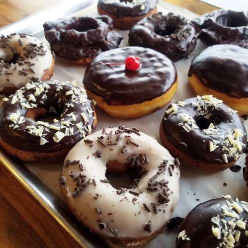 A tray of assorted donuts, featuring chocolate-glazed, white icing, and topped with sprinkles and a cherry.