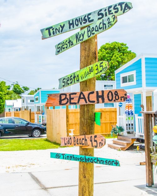 Colorful wooden signs on a post indicate distances to various locations, including Siesta Key Beach and Lido Beach.