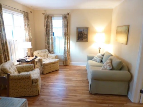 Cozy living room with two patterned armchairs, a sofa, wooden floor, and soft lighting from a lamp.
