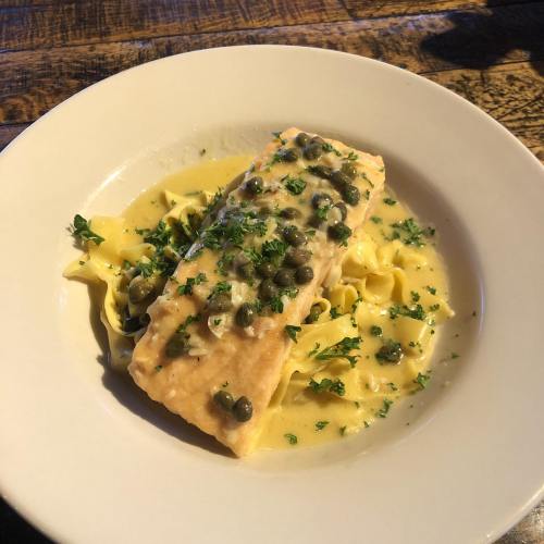 A plate of salmon topped with capers and herbs, served over fettuccine in a creamy sauce.