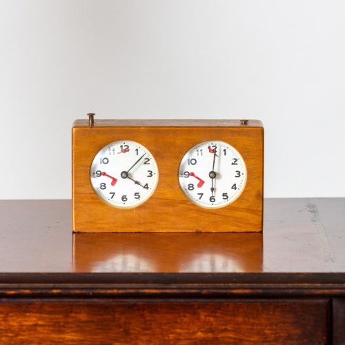 A vintage wooden clock with two round faces displaying different times, placed on a wooden surface.