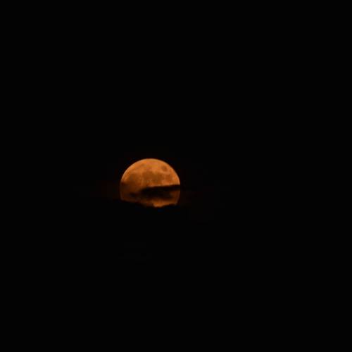 A glowing orange moon partially obscured by dark clouds against a black sky.