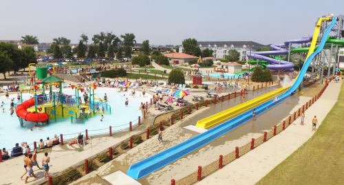 A vibrant water park with slides, a children's play area, and families enjoying the pool on a sunny day.