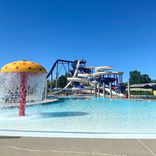 A vibrant water park scene featuring a large water slide and a splash pad under a clear blue sky.