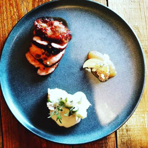 A plate featuring sliced meat, a dollop of creamy sauce, and a small portion of mustard, all artfully arranged.