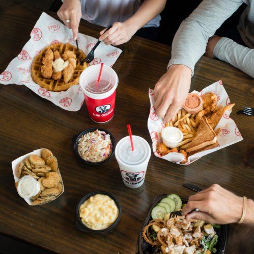 A table with various fast food items, including fried chicken, fries, coleslaw, and drinks, shared by two people.
