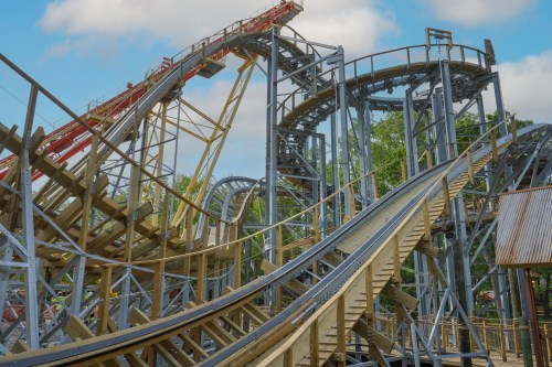 A wooden roller coaster with twisting tracks and steep drops under a blue sky.